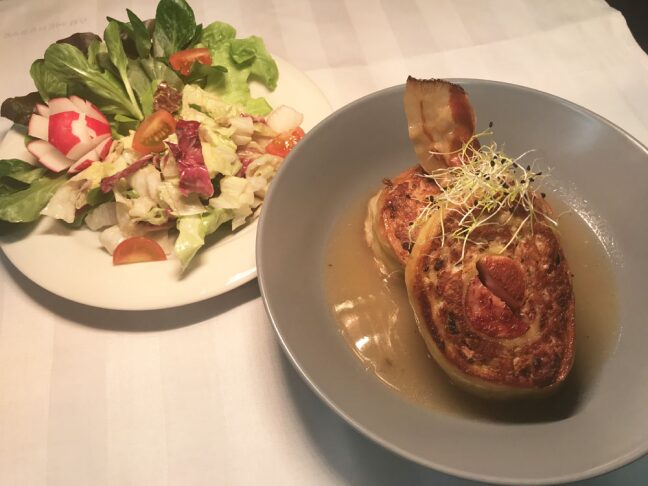 Assiette de fleischnacka de choucroute disposé à côté d'ne assiette de salade composée sur une nappe blanche