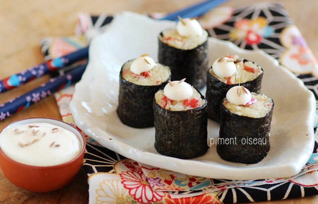 Cinq sushis de à la choucroute disposés sur une assiette, avec un petit bol de sauce à côté