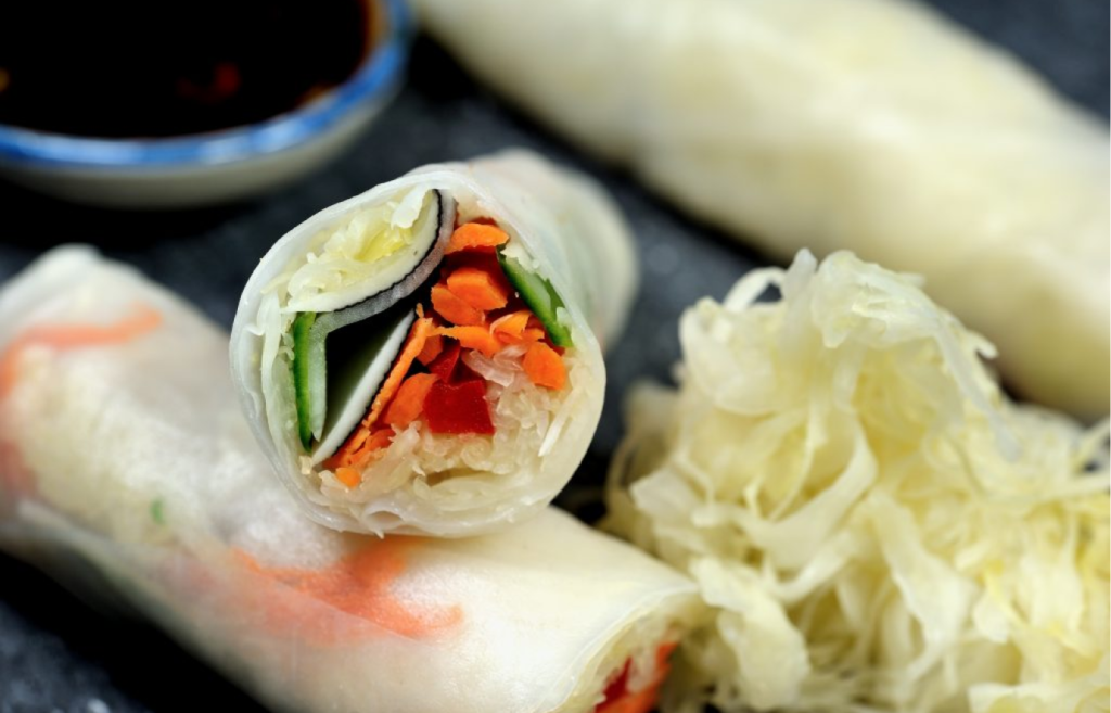 Deux rouleaux de printemps à la choucroute disposés sur une ardoise avec une salade de choucroute